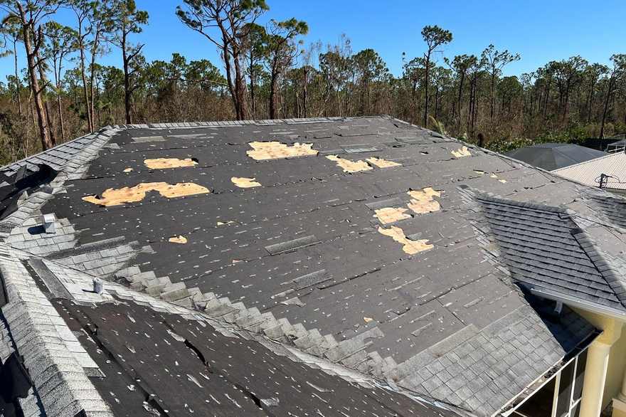 Storm-damaged asphalt roof with missing shingles and exposed deck